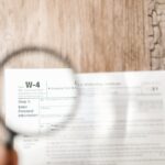 Close-up of a W-4 tax form through a magnifying glass on a wooden table.