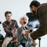 An excited senior woman experiencing virtual reality with the help of two young men indoors.