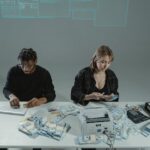 Two people counting money at a desk with computers and cash equipment.